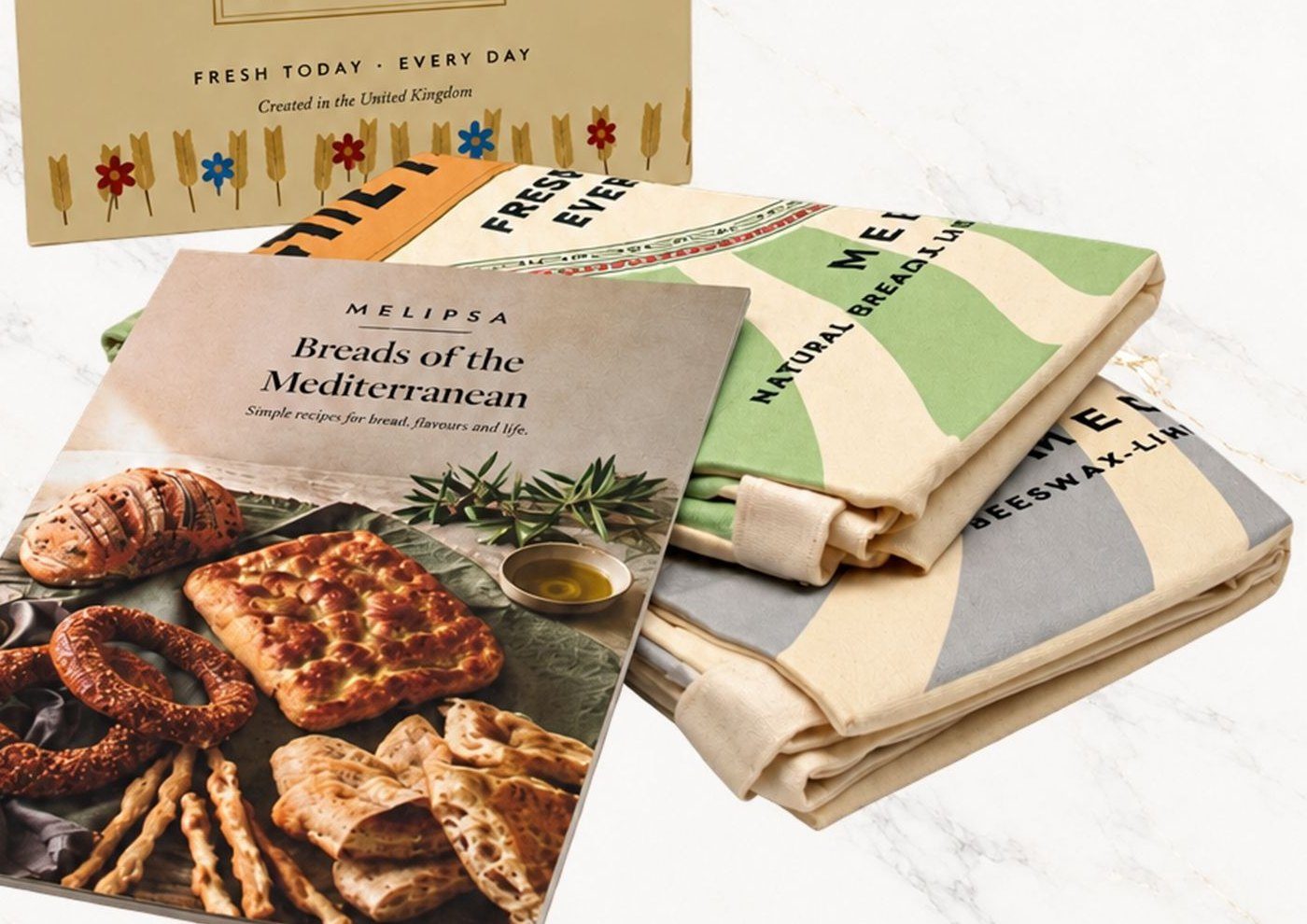 Two folded Melipsa bread bags, one green and one grey, with the recipe book